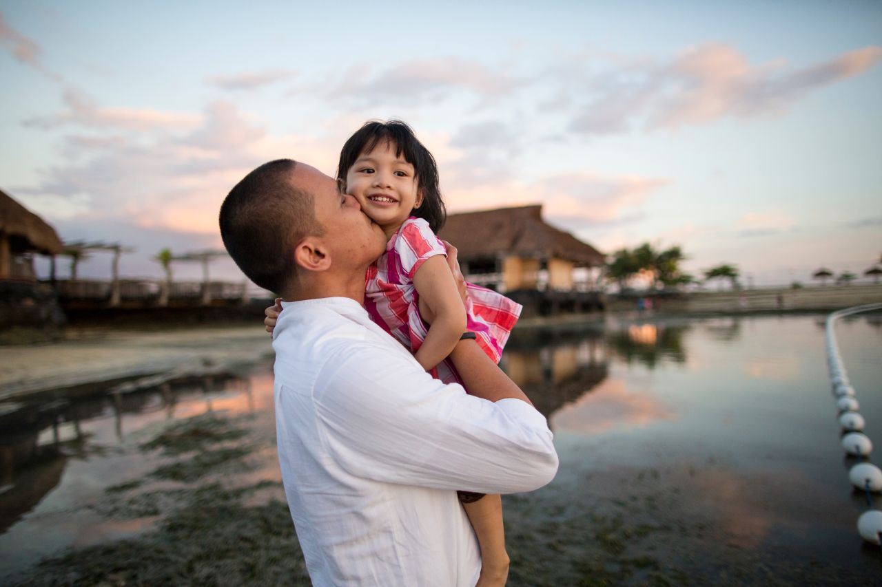 A father holds his young daughter at a beach