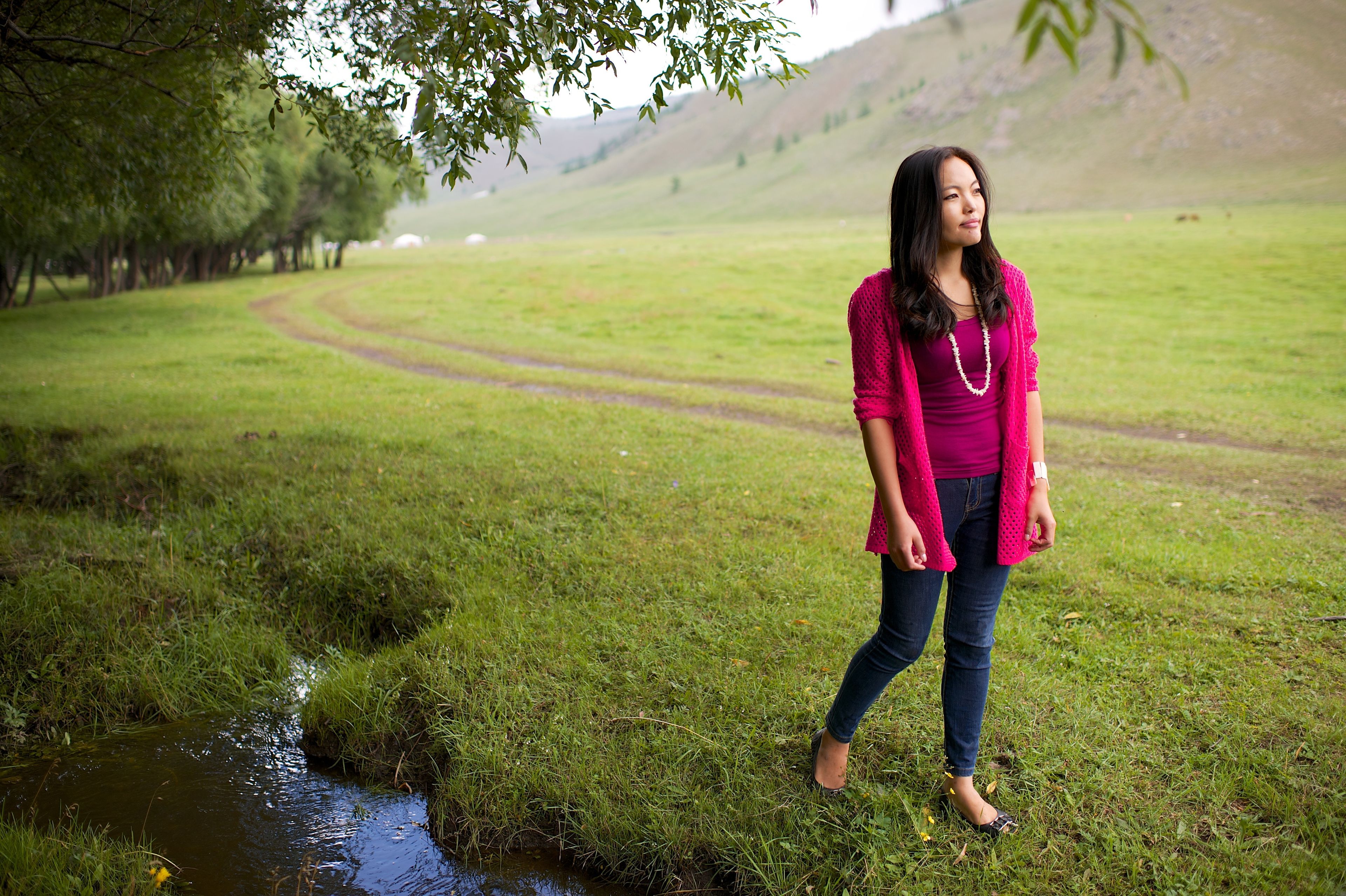 A Mongolian woman stands in a field, pondering.
