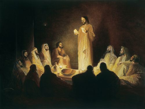 Christ in a white robe, standing in front of His Twelve Apostles in a dark room, illuminated by a few lamps while breaking bread.