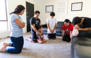 A couple kneels in prayer with their children in their family room
