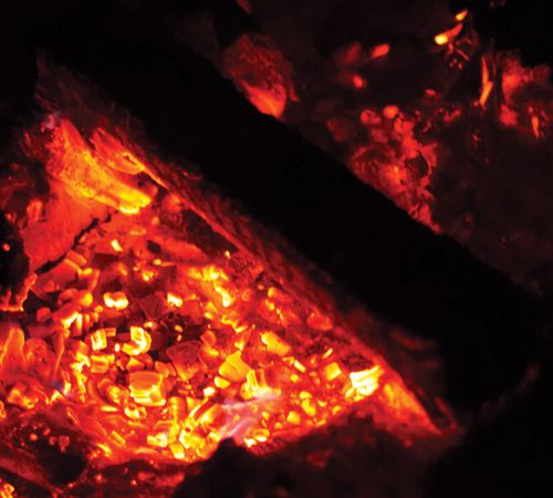 A photograph of red embers glowing in a fire pit on a dark night.