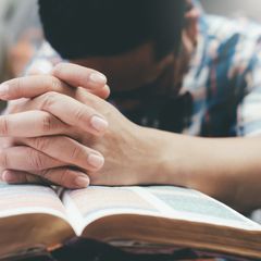 A man prays with his hands resting on an open bible.