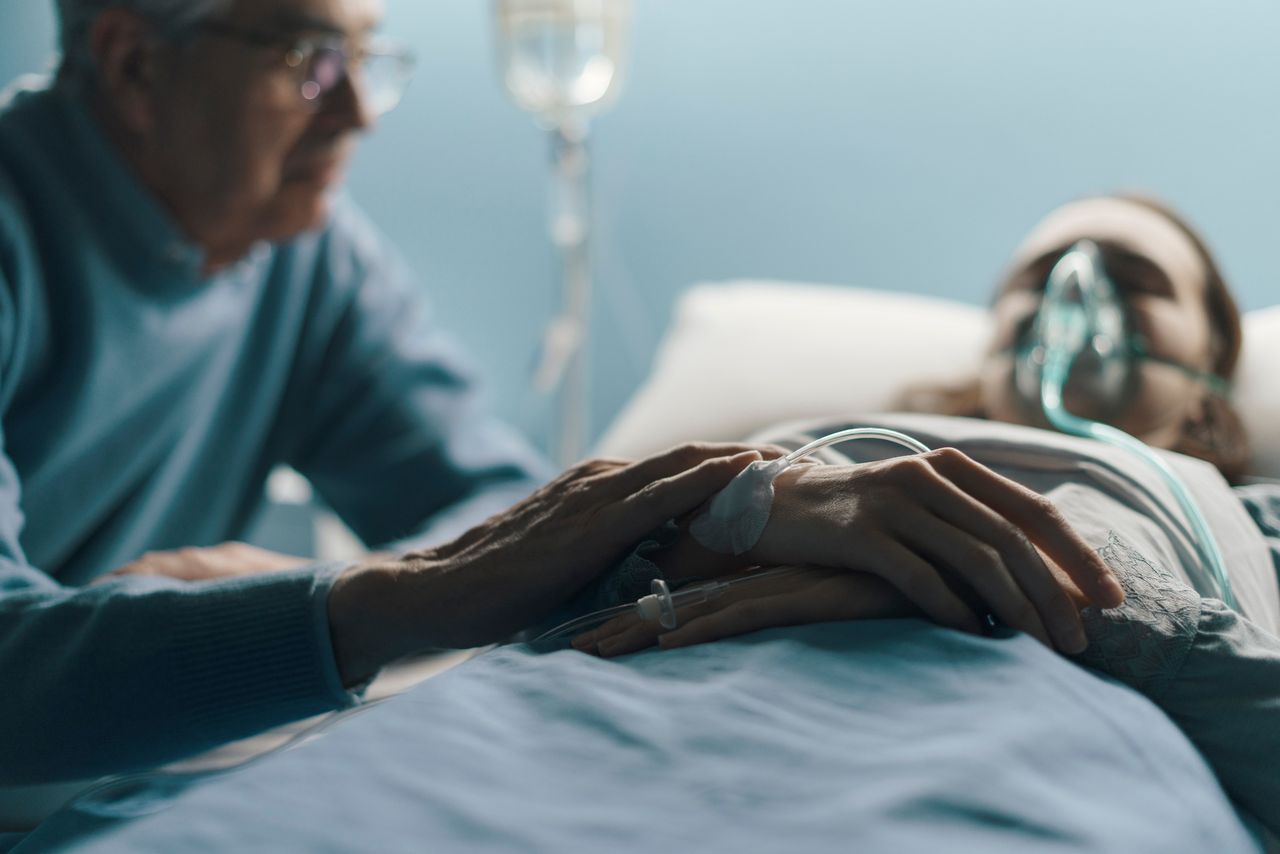 Um homem se senta ao lado de uma mulher em uma cama de hospital