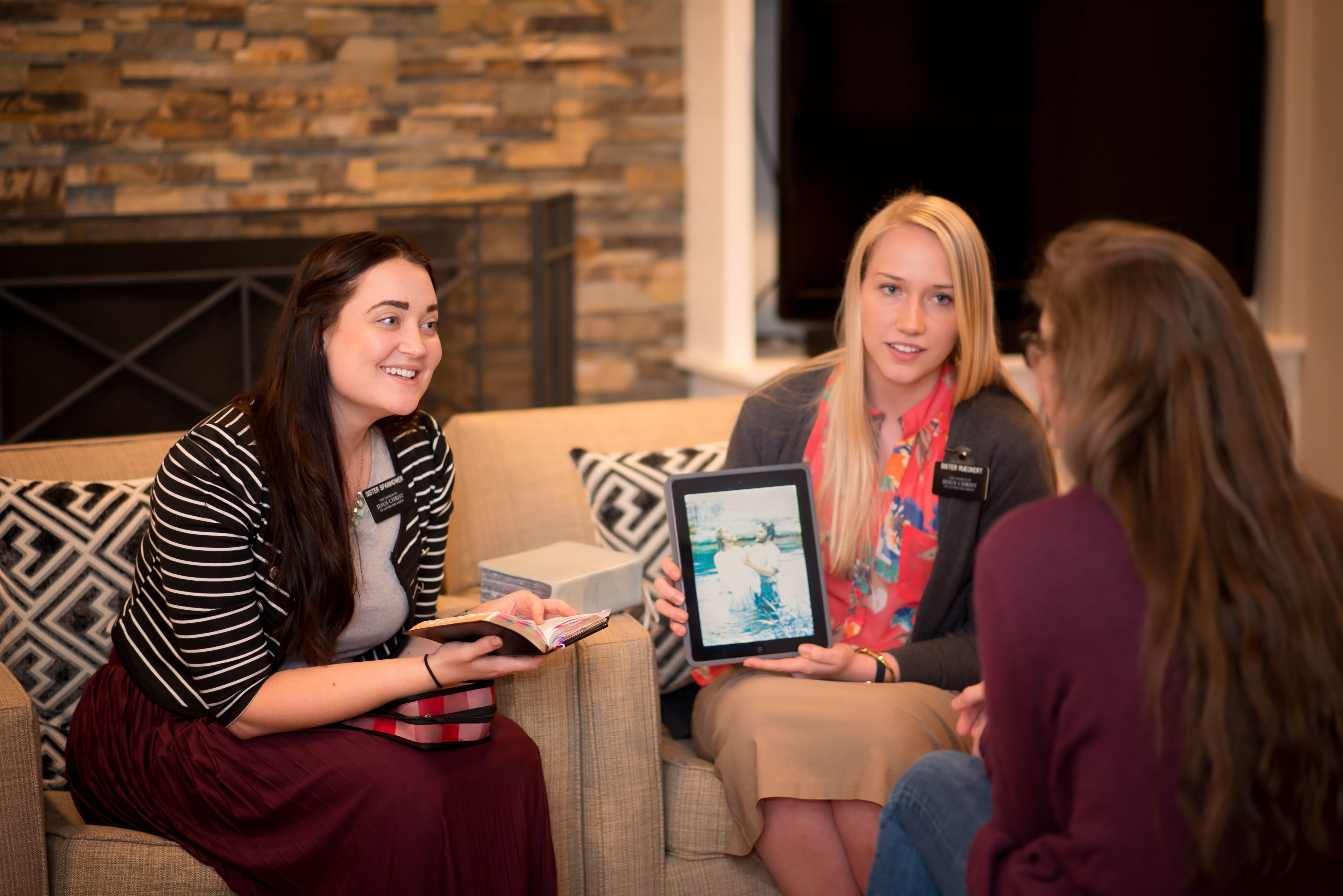 Two sister missionaries teaching a woman with their scriptures and an iPad.