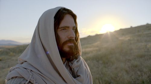 Jesus is standing on a hill. You can see the sun in the background