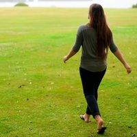 A young woman or young adult woman walking across a lawn.