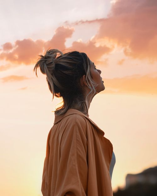nuori nainen katsomassa ylöspäin oranssiin auringonlaskuun
