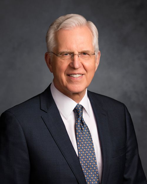 Porträtfoto von Elder Neil L. Andersen mit schwarzem Anzug und roter Krawatte vor einem grauen Hintergrund