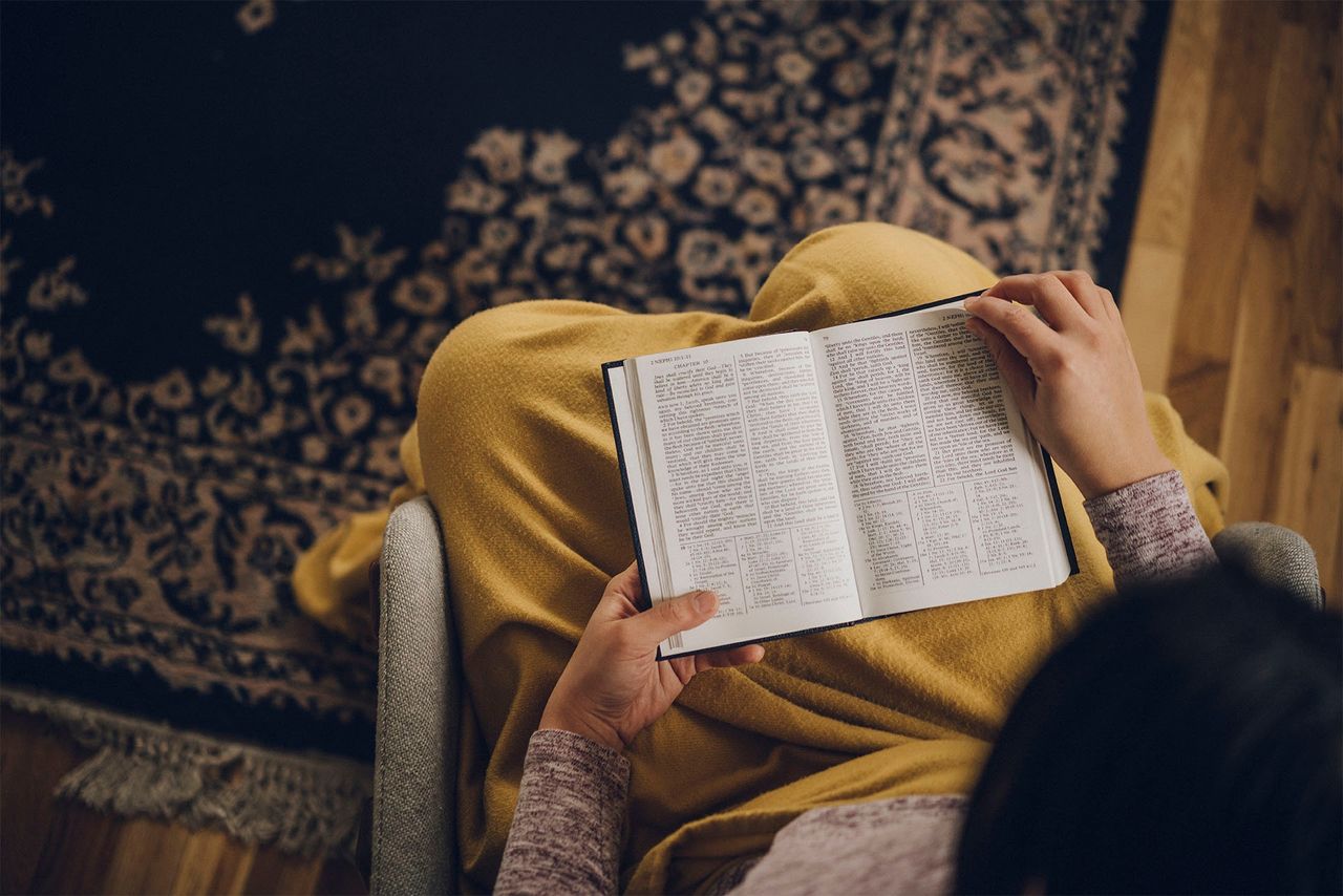 A woman studies the Book of Mormon while sitting in chair with a blanket