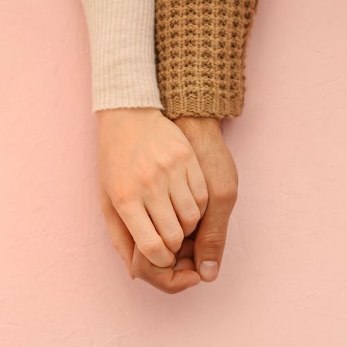 two hands clasped over a pink background