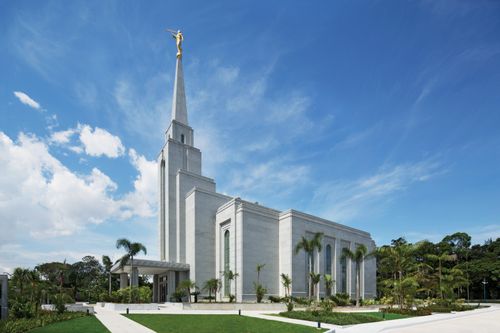 A side view of the Manaus Brazil Temple, with palm trees growing on the grounds and large white clouds overhead.