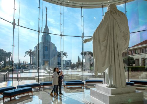 a couple holding a child while looking at the Christus statue in the Rome Italy Temple Visitors’ Center