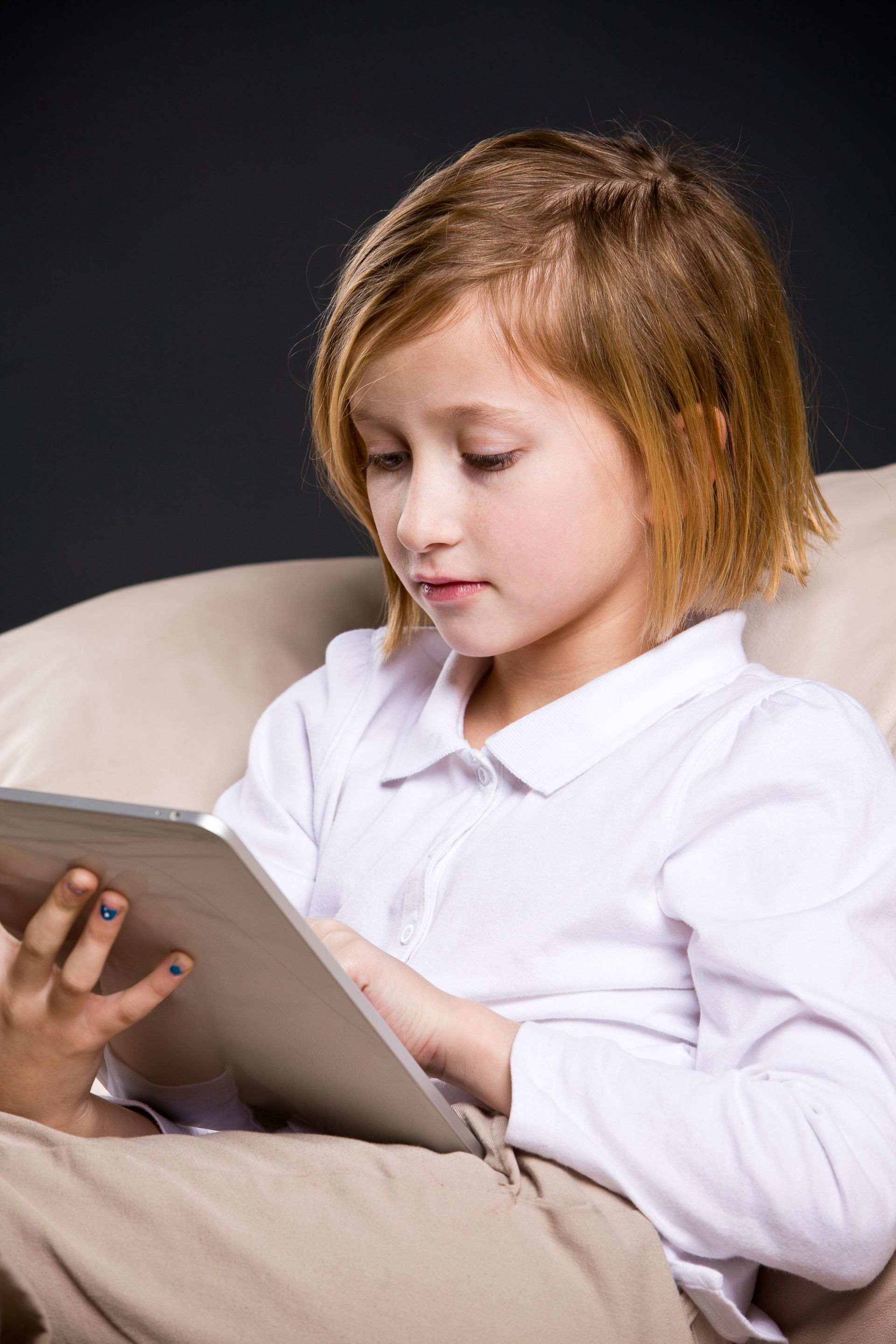 A young girl sits and looks at a tablet.