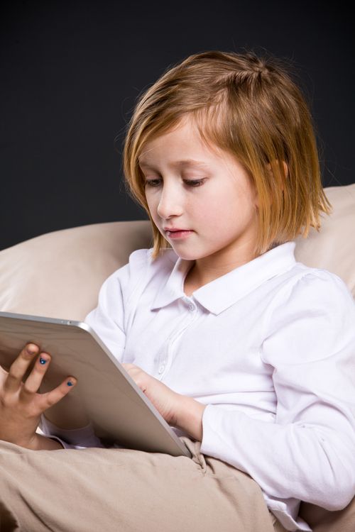 A young girl sits in an armchair and scrolls through a tablet.