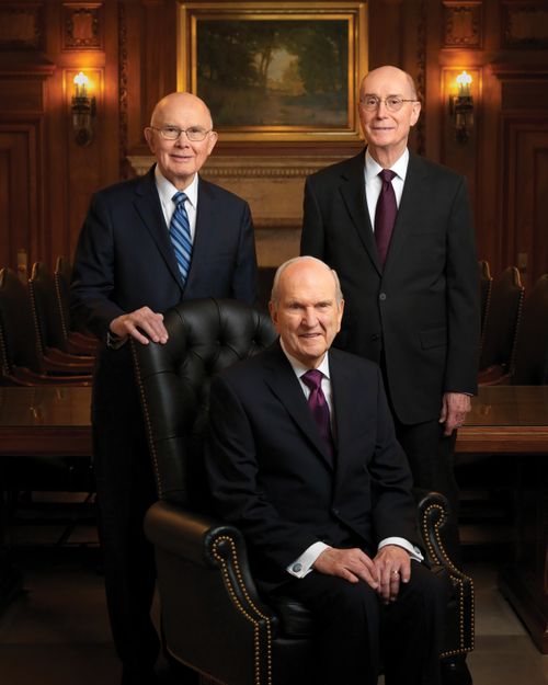 Портрет Первого Президентства: Президент Рассел М. Нельсон сидит на стуле, президент Даллин Х. Оукс и президент Генри Б. Айринг стоят сзади него.