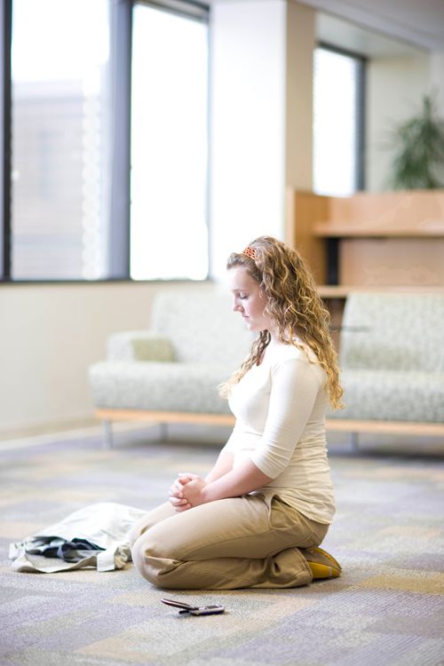 A young woman with curly blonde hair kneeling in a room and praying.