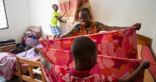 Ghanan brothers help each other with chores by making the beds and folding sheets.