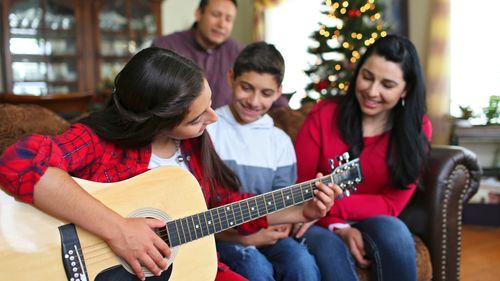 A young woman plays the guitar for her brother and parents at Christmastime.
