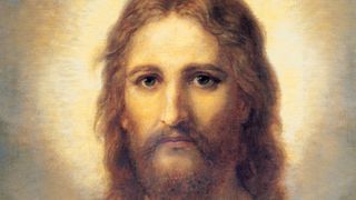 Frontal head and shoulders portrait of Jesus Christ. Christ is depicted wearing a pale red robe with a white and blue shawl over one shoulder. Light emanates from His face.