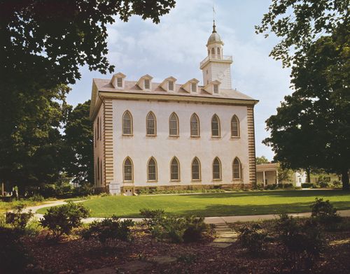 A side view of the Kirtland Temple, framed by large green trees on the sides.