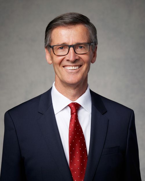 A portrait of Steven J. Lund wearing a dark-blue suit and a red tie, in front of a gray background.