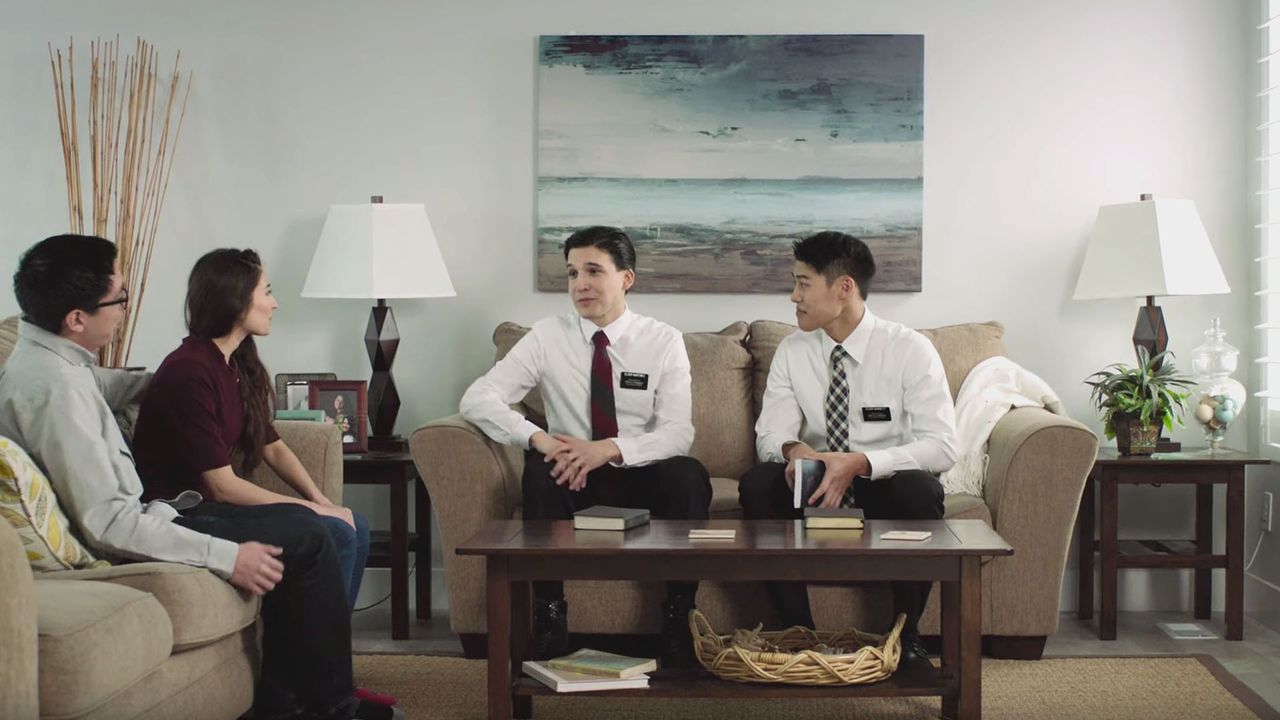 Uma dupla de élderes ensina um casal na sala de estar deles