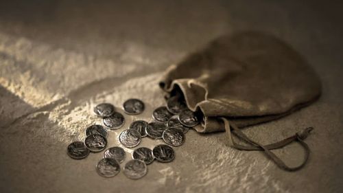A small leather bag spilling small silver coins over a stone surface.