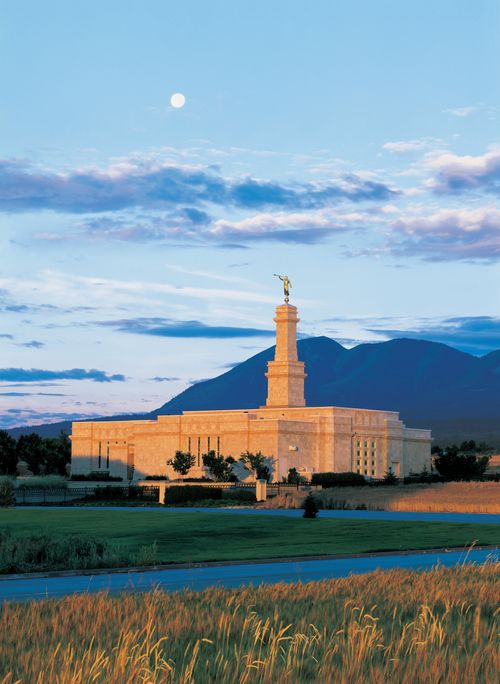 A view from afar of the Monticello Utah Temple in the evening, with the moon barely visible above the clouds.