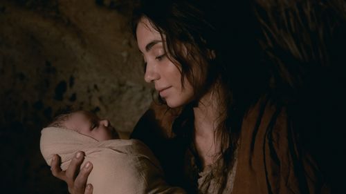An actress is portraying Mary the mother of Jesus. She is holding the baby Jesus in her arms and looking at him.