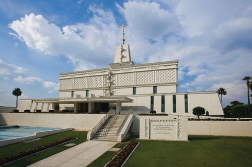 A view of the front and entrance of the Mexico City Mexico Temple, with large white clouds overhead and a green lawn in the foreground.