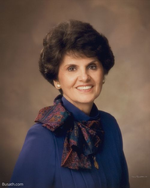 A photograph of Ardeth Greene Kapp against a brown background, wearing a blue blouse and a patterned scarf around her neck.