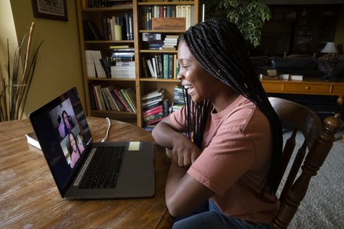 A young woman sits in her home. She has her computer open and she teaches various people online.