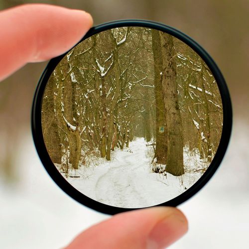 Dedos sosteniendo un filtro polarizador circular frente a un paisaje invernal