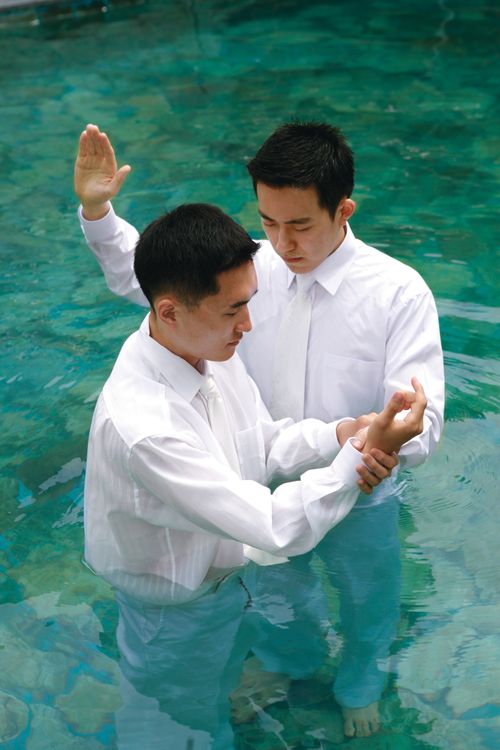 A young man being baptized by another man.  They are both Korean.
