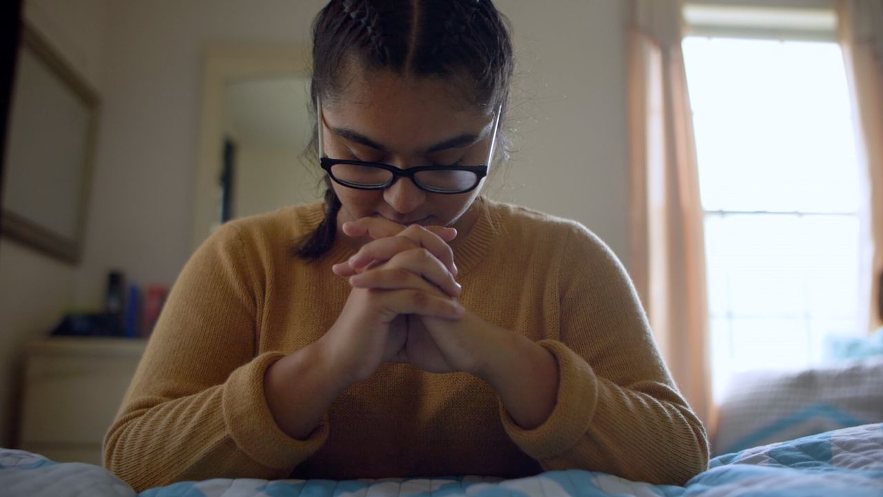 Foto de joven orando orando de rodillas junto a su cama