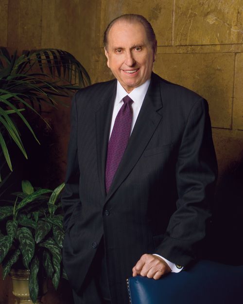 A portrait of President Thomas S. Monson in a black suit and purple tie, standing with his arm resting on a blue chair and with green plants to the left.