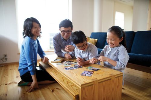A young Japanese boy and girl and their parents looking at photographs on a table. 