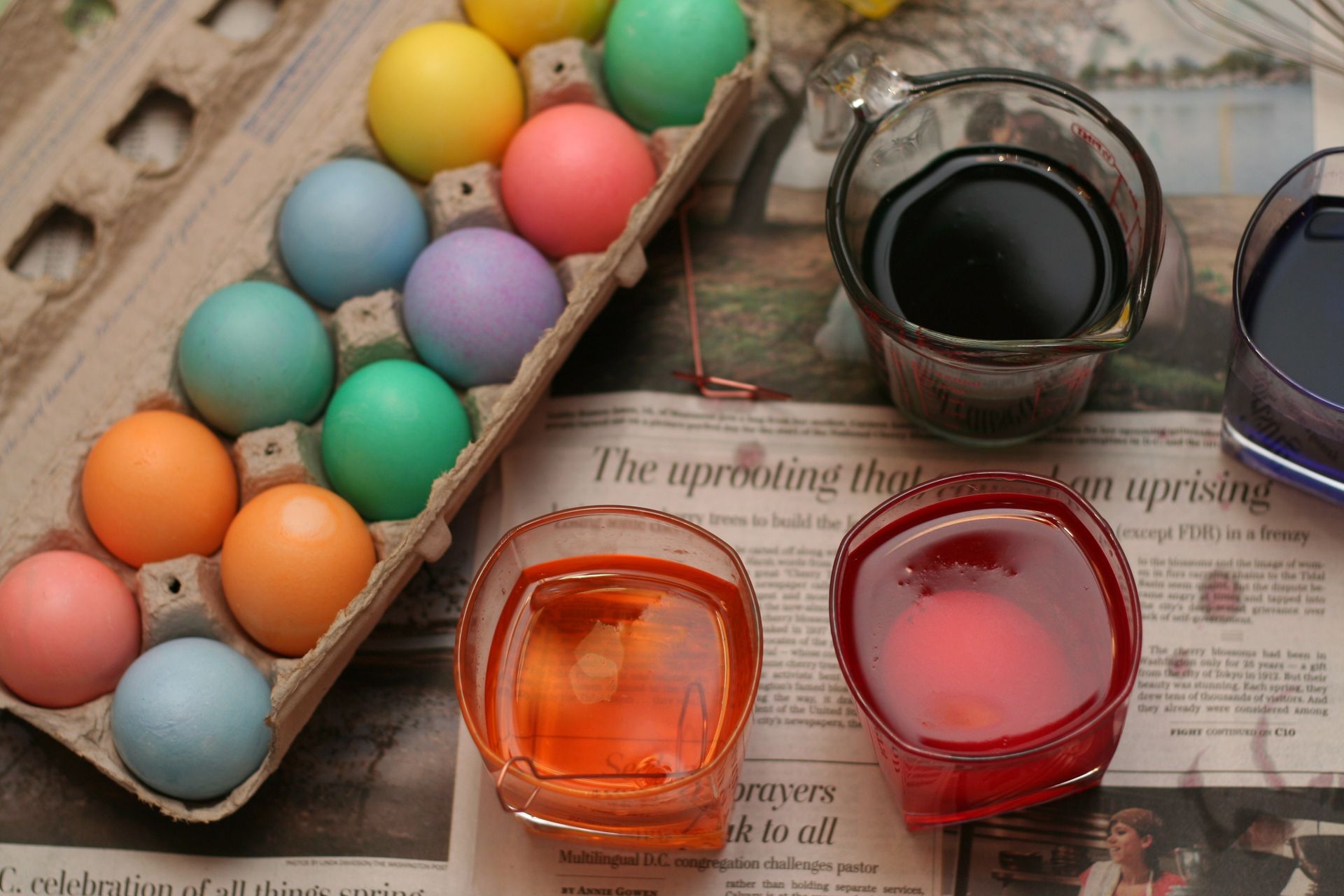 Several cups of Easter egg dye near a carton of newly colored eggs.