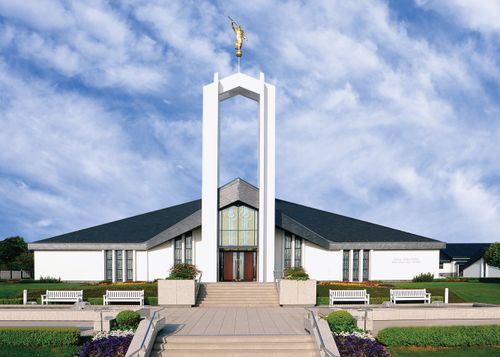 A view of the front of the Freiberg Germany Temple, with a bright blue sky and thin white clouds above the spire.