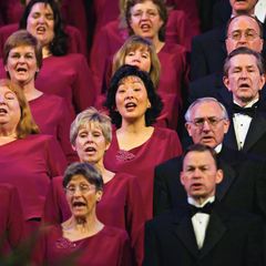 Women in maroon dresses and men in white shirts, black suits, and black bow ties, singing in the Mormon Tabernacle Choir.