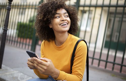 young woman holding phone while sitting on curb