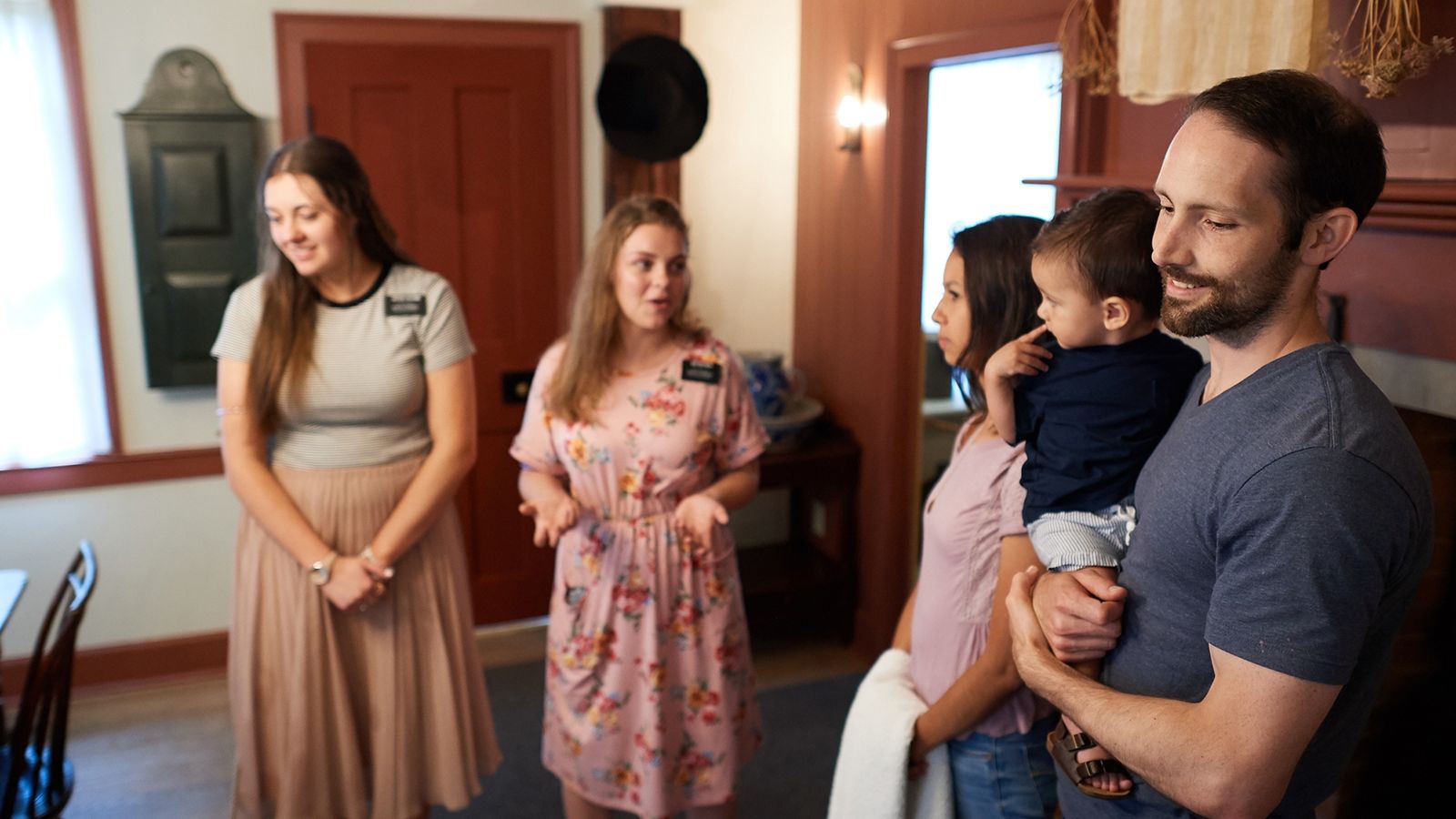 Various people visit the Kirtland Visitors Center. They look at art and artifacts that are up on the walls and around the homes and rooms.