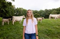 A young woman stands outside in a field in Kentucky. She is near cattle.