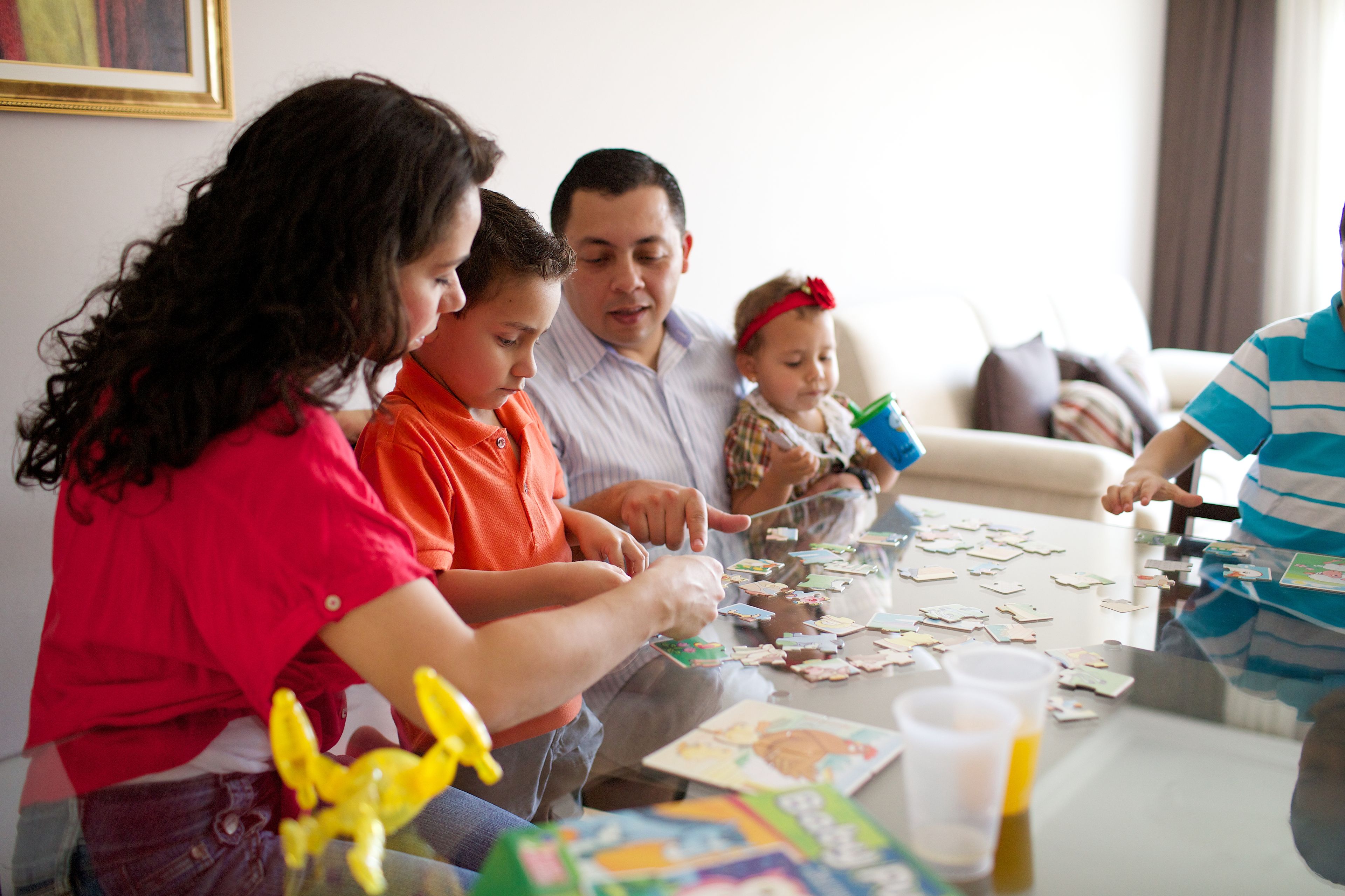 A family sits together at a table in their home and builds a puzzle.  