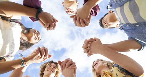 En gruppe unge menn og unge kvinner i sirkel holder hverandre i hendene og smiler til hverandre for å oppmuntre hverandre.