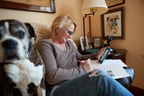 A woman studies the gospel using a phone and magazine while sitting on her couch next to her dog.