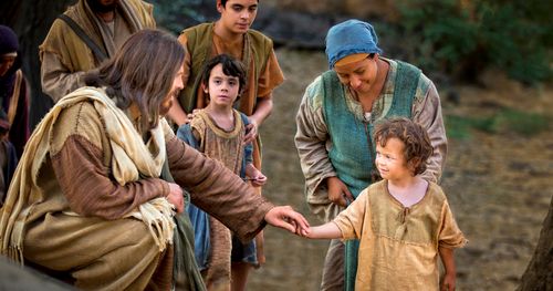 Actor portrays Jesus loving a child as He stoops to touch the child's hand.