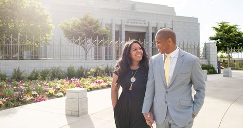 Couple walks past Draper Utah Temple while holding hands and looking lovingly toward each other.