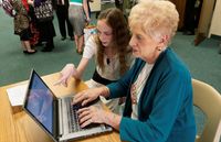 youth helping elderly woman use a laptop