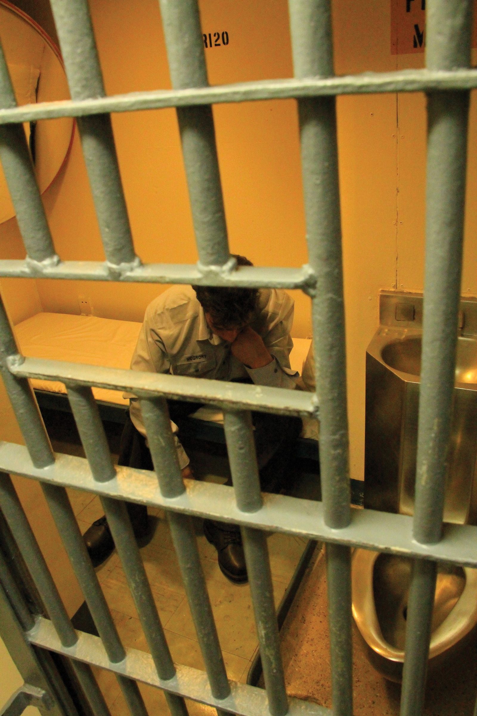 A man sitting in a prison cell looking discouraged.